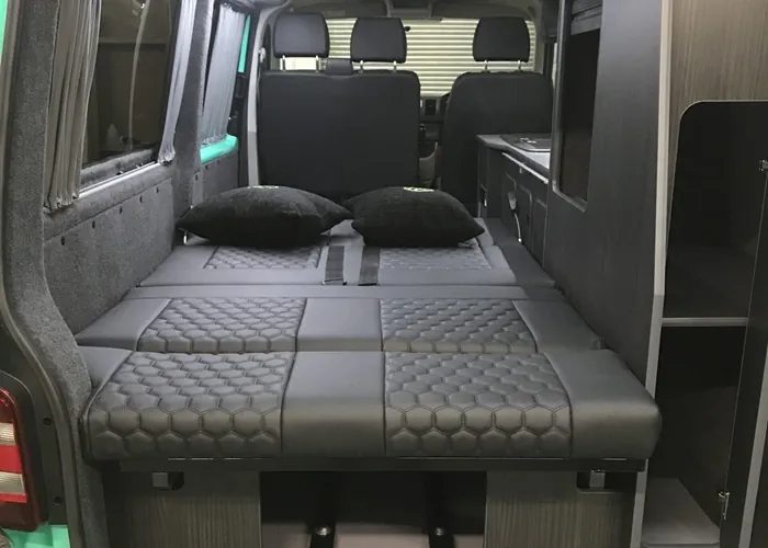 Camper van interior featuring a folded-out bed with pillows and integrated storage solutions