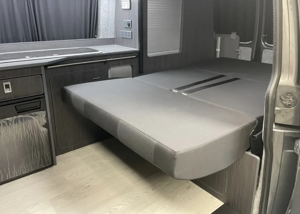 Camper van interior with a folded-out bed and kitchenette, showcasing bespoke design for comfort and utility