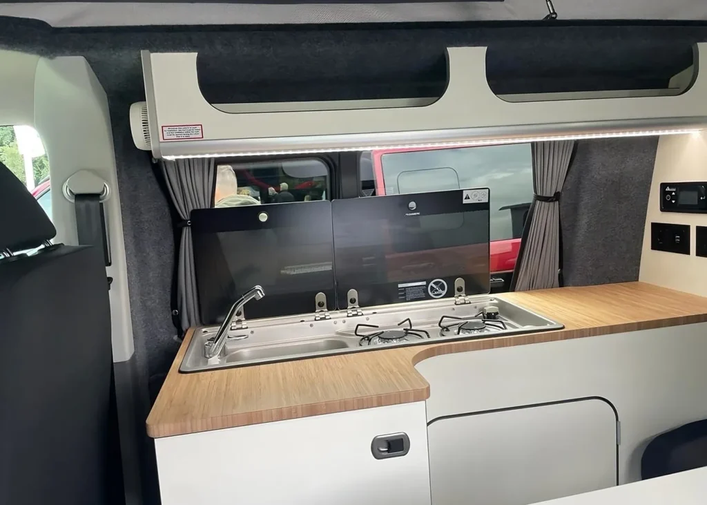 Compact camper van kitchen with a sink and stove, showcasing efficient design in bespoke conversions