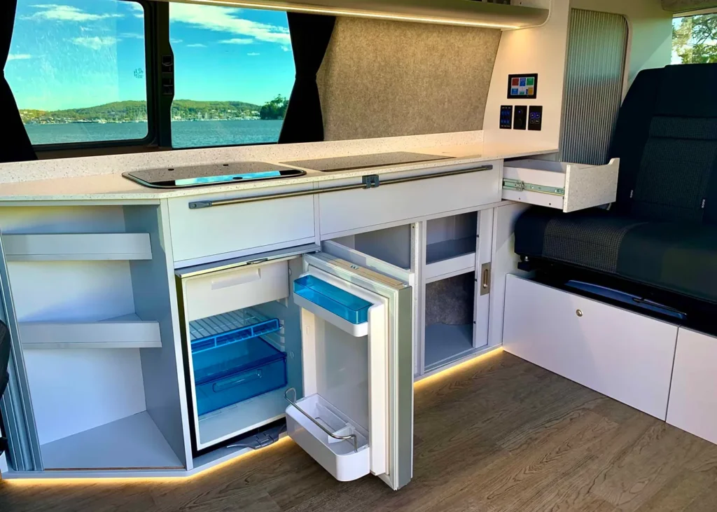 Modern camper van kitchen with sink, stove, and fridge, showcasing premium camper conversions.