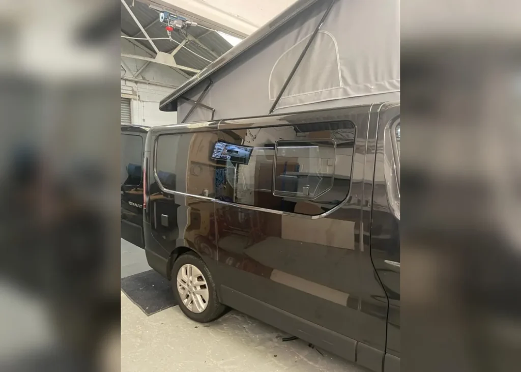 Black camper van with an extended pop-up roof, side view taken indoors during conversion process