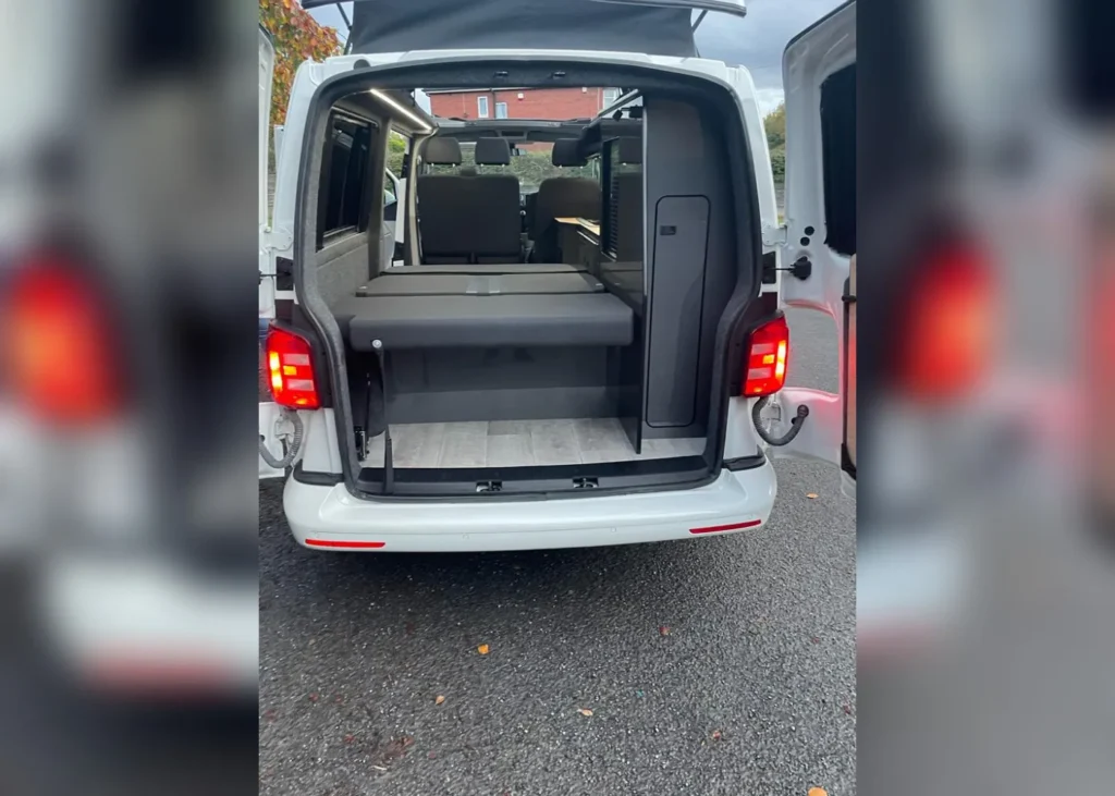 Rear view of a white camper van with an open door, part of bespoke camper conversion projects in Manchester