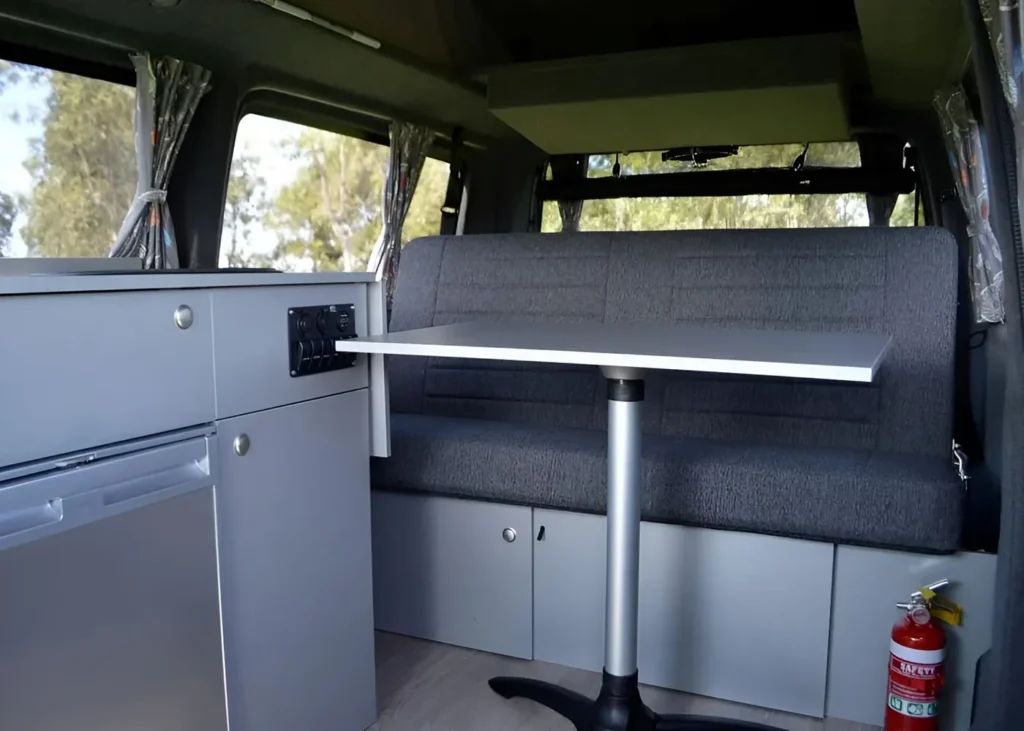 Interior view of a camper van dining area with a sleek table and bench seating, designed for comfort and practicality during travels