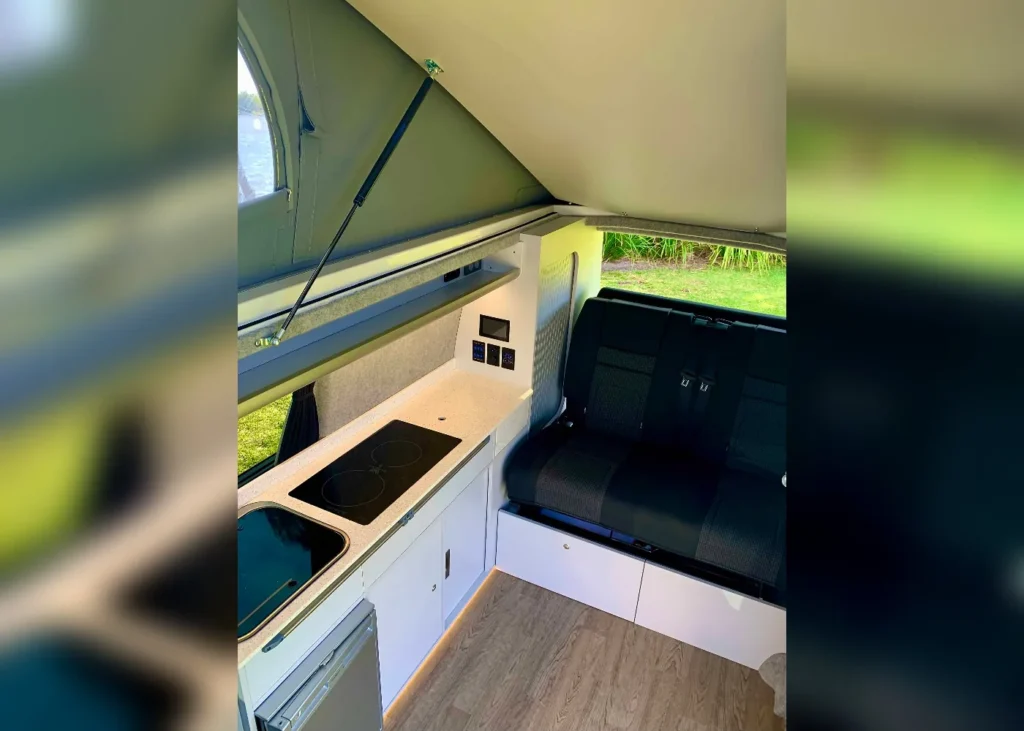 Camper van kitchen with induction cooktop, sink, mini-fridge, and seating area