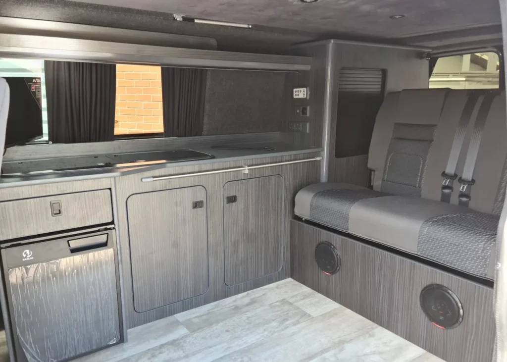 Camper van interior with kitchen cabinets, refrigerator, and lounge seats