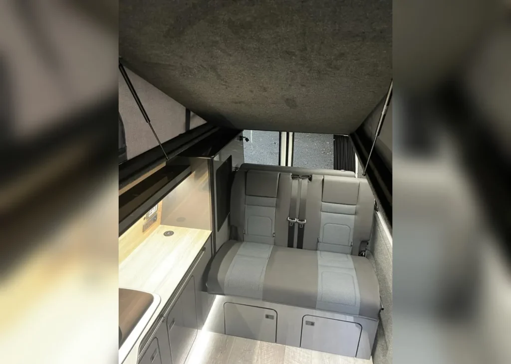 Camper van interior with pop-up roof, seating, and kitchen area