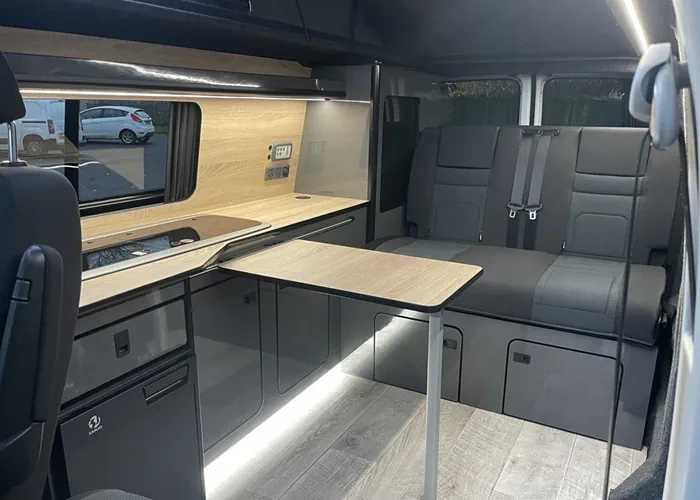 Customized camper van interior with a foldable table, kitchenette, and modern seating