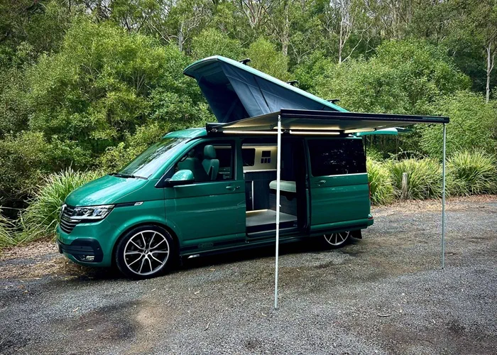 Green camper van with extended awning in a forest setting