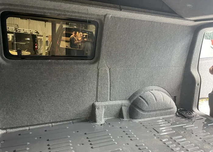 Camper van interior with partial conversion, showing insulated walls and a window installation in progress