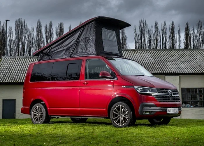 Red camper van with an extended pop-top roof, parked outdoors on green grass