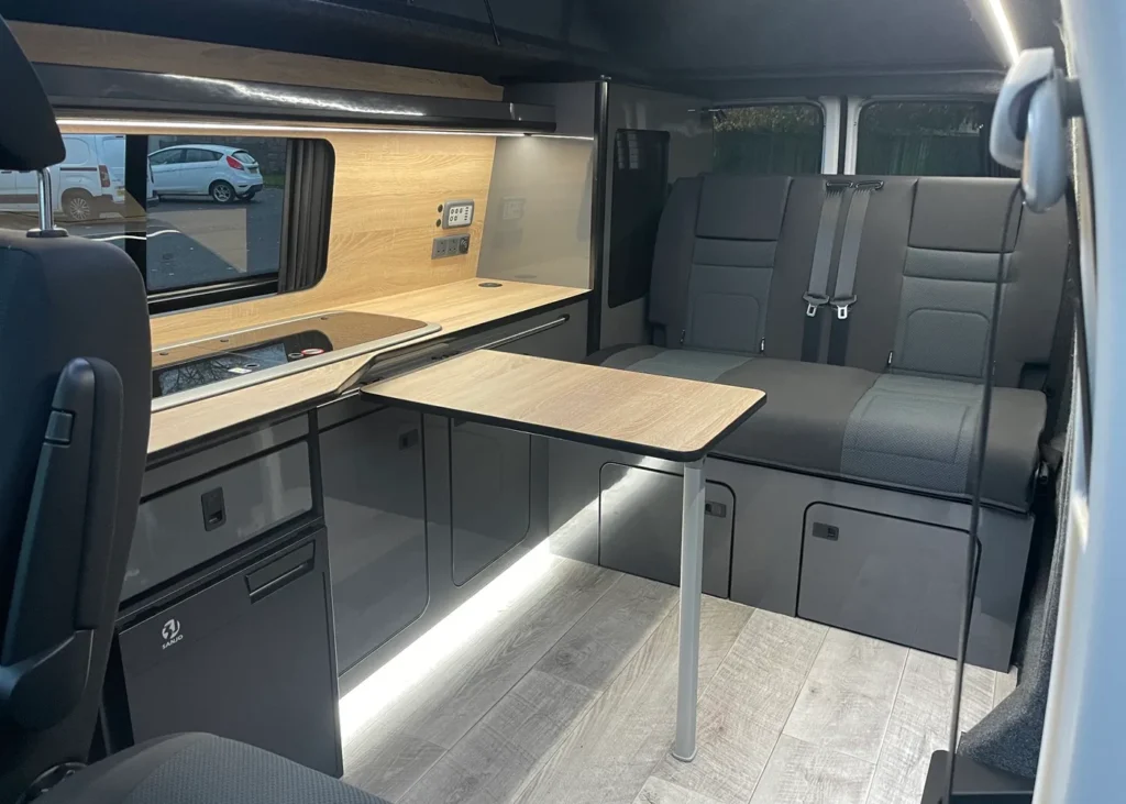 Modern VW camper interior with kitchen, seating, and table