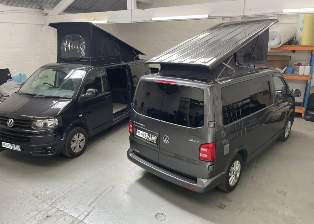 Two campervans with pop-up roofs in a workshop