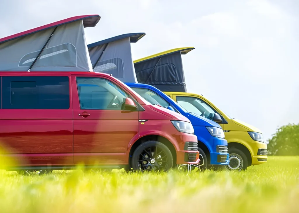 Colorful camper vans with pop-top roofs parked on a grassy field - Contact camper conversion experts in Manchester at HAWKE VANS