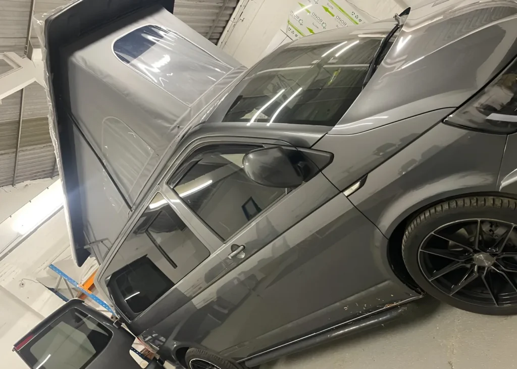 Gray camper van with pop-up roof extended inside a workshop