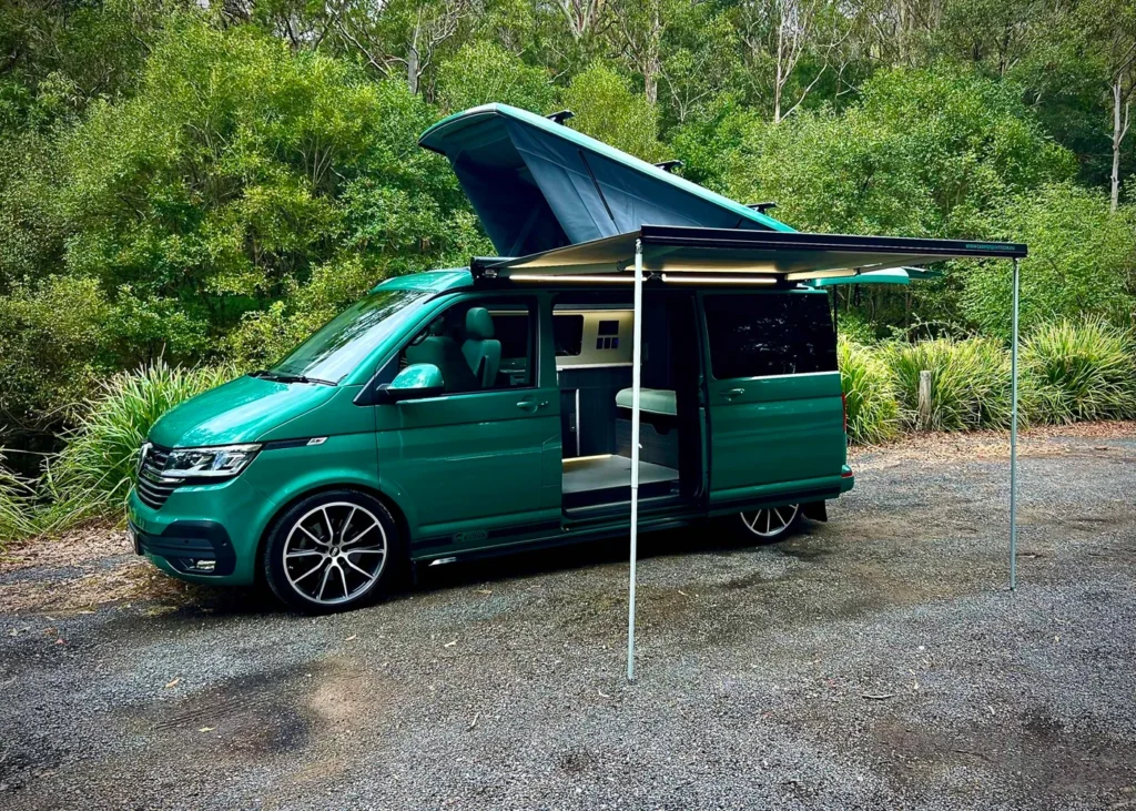 Green camper van with pop-up roof and awning in a forest setting