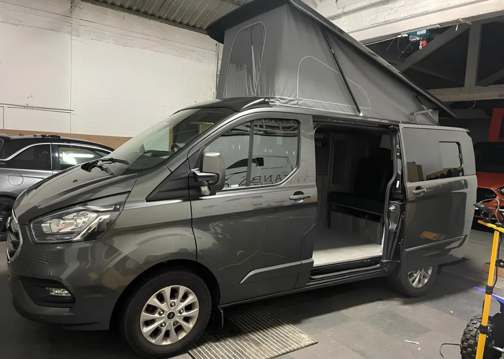 Grey camper van with a pop-up roof and sliding door open, showcasing the interior