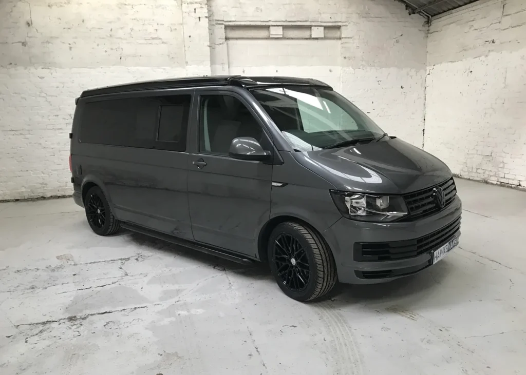 Side view of a grey Volkswagen camper van with black wheels and tinted windows, parked in an indoor workshop