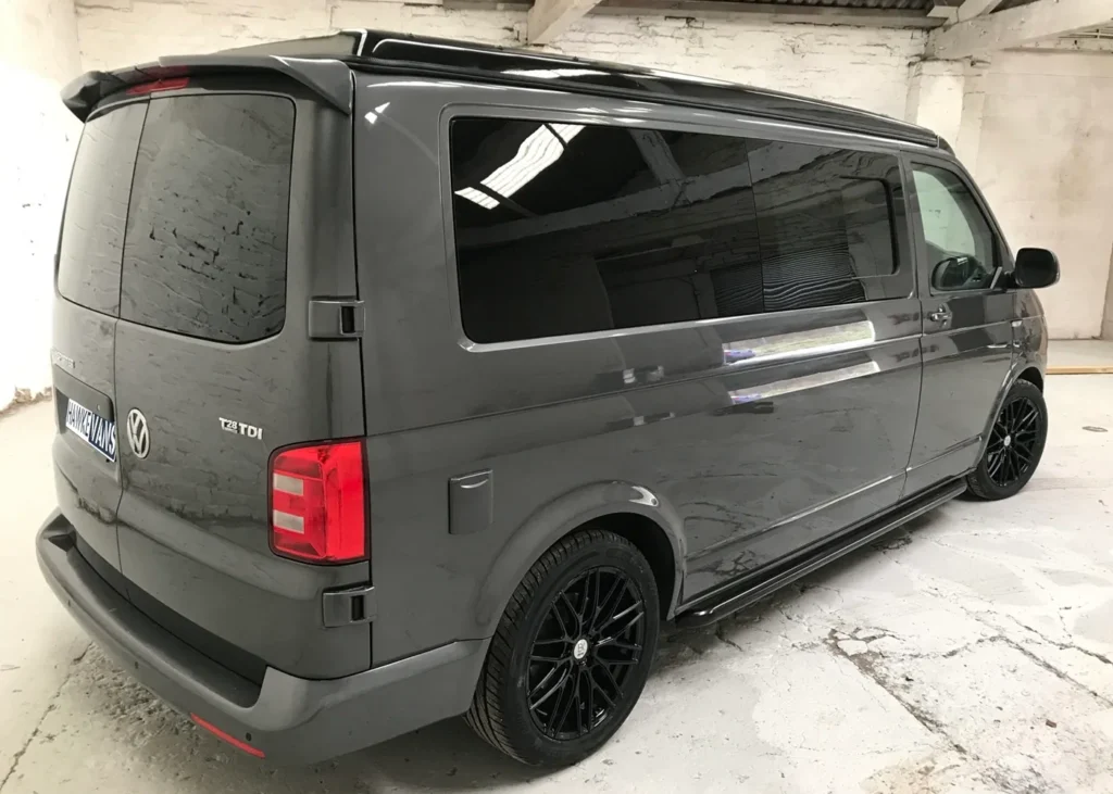 Side view of a grey Volkswagen camper van with black wheels and tinted windows, parked indoors