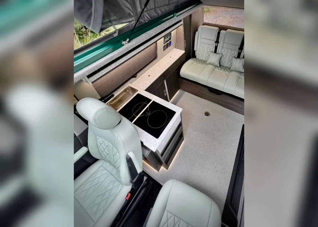 Interior of a luxury camper van with white quilted leather seats, modern kitchen appliances, and ambient lighting