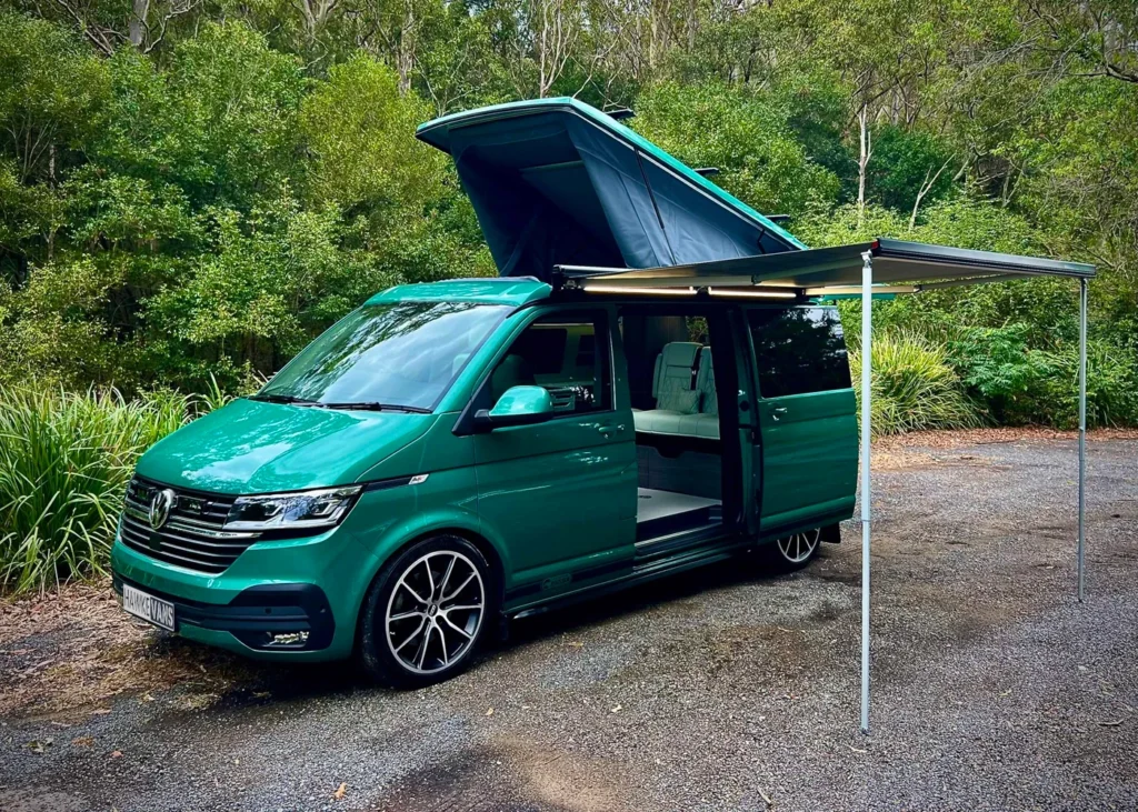 Mint green camper van with a pop-up roof and awning in a forest setting