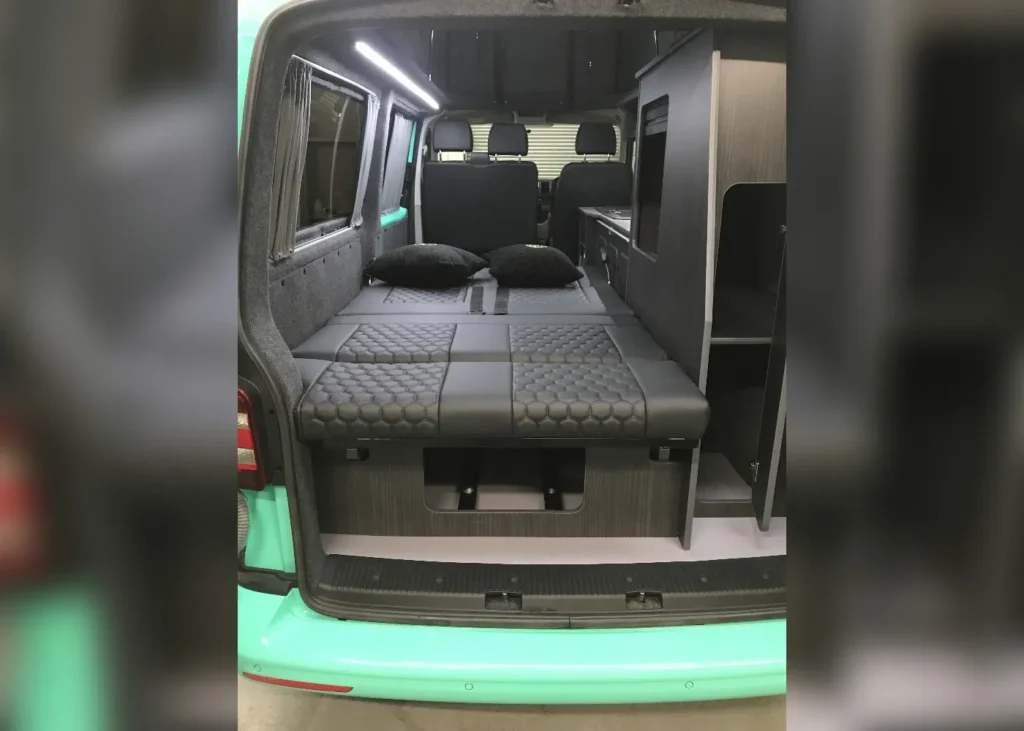 Interior of a mint green camper van with a fold-out bed and hexagonal-patterned upholstery