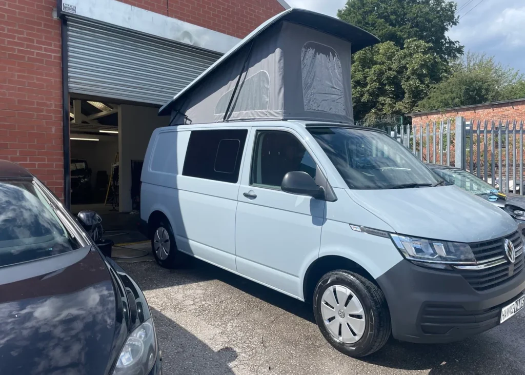 White camper van with a pop-up roof outside a workshop