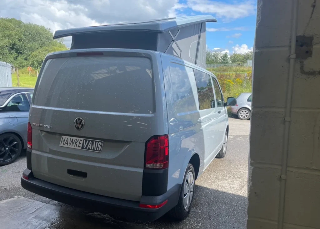 Rear view of a white VW camper van with a raised roof in a sunny outdoor setting