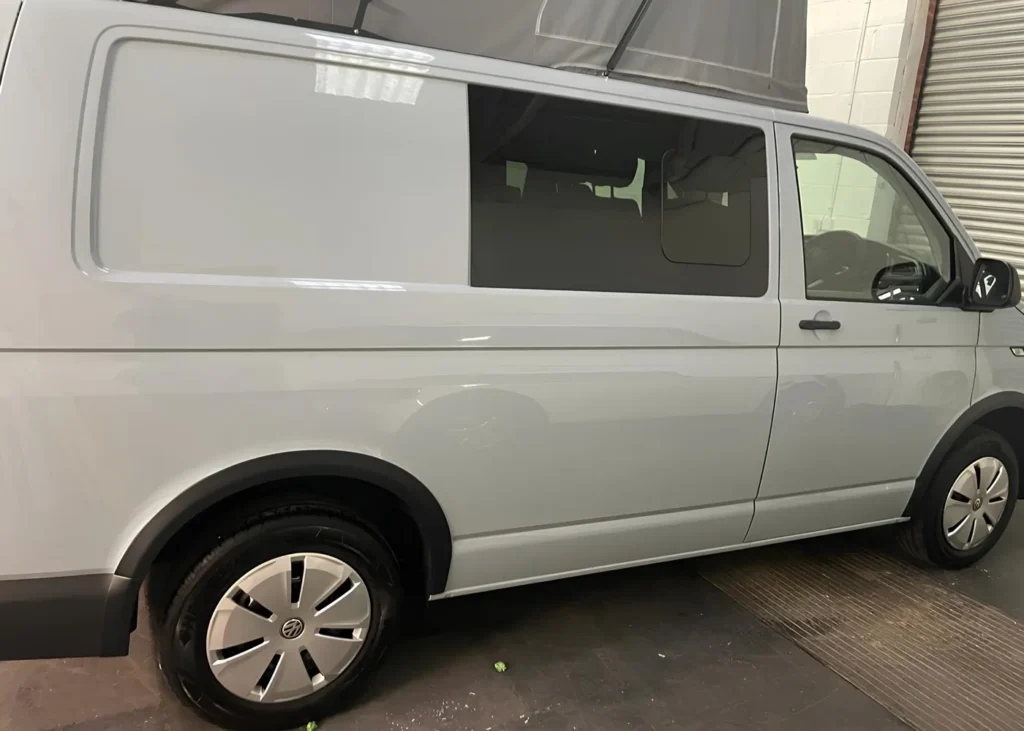 Side view of a white van conversion with pop-up roof and tinted windows