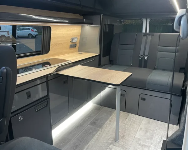 Modern VW camper interior with kitchen, seating, and table