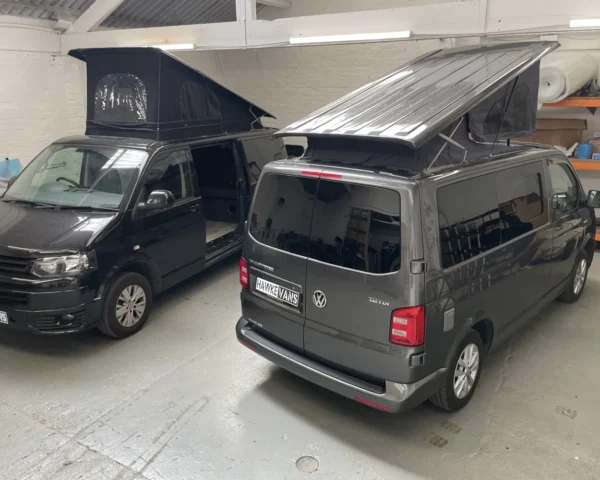 Two campervans with pop-up roofs in a workshop