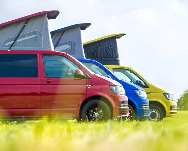 Colorful camper vans with pop-top roofs parked on a grassy field - Contact camper conversion experts in Manchester at HAWKE VANS