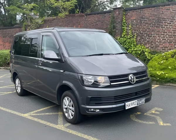 Grey camper van parked in an outdoor area with a brick wall and greenery in the background