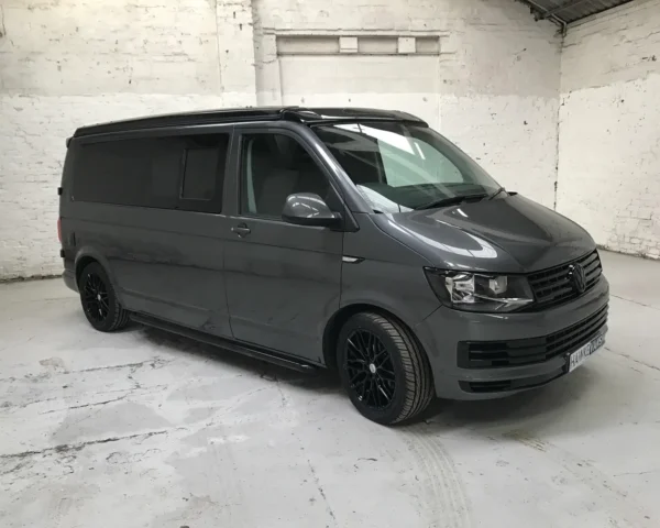 Side view of a grey Volkswagen camper van with black wheels and tinted windows, parked in an indoor workshop