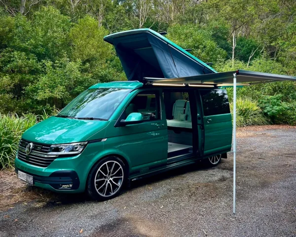 Mint green camper van with a pop-up roof and awning in a forest setting